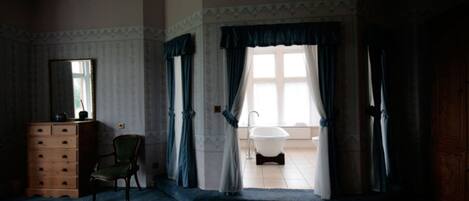 A room with a wooden dresser, a chair, a bathtub, and a window with curtains.