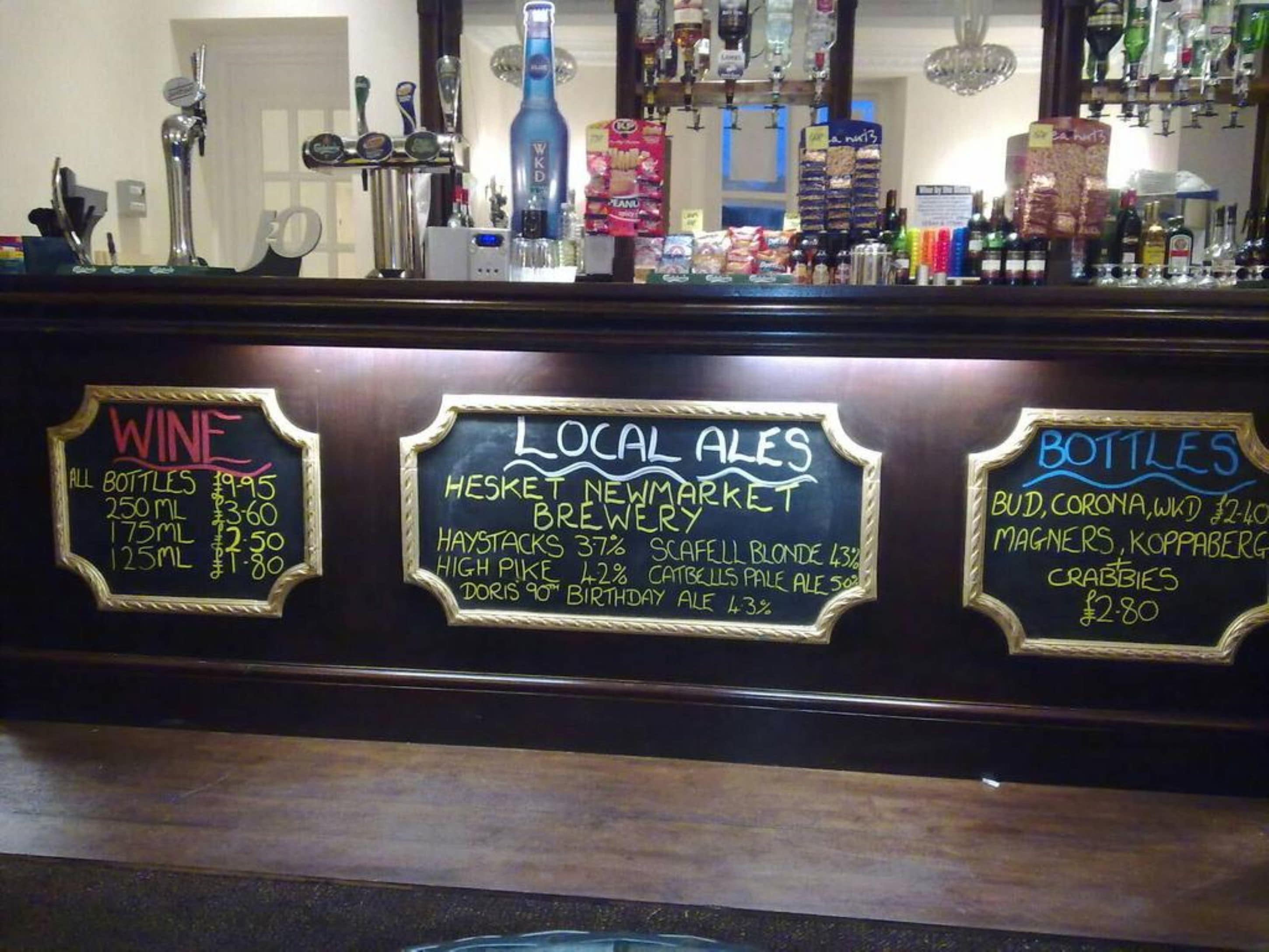 Una barra con carteles de pizarra que indican los precios de vino, cervezas locales y botellas.