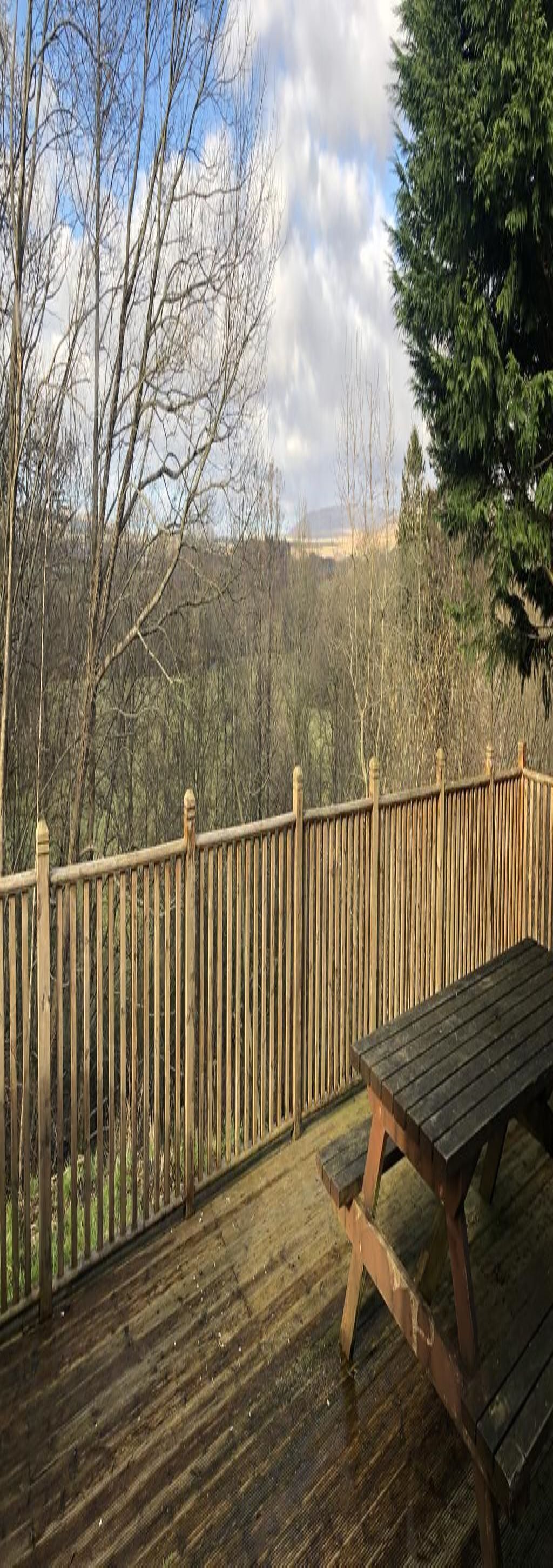 Una terraza de madera con un banco, rodeada por una valla de madera y árboles.