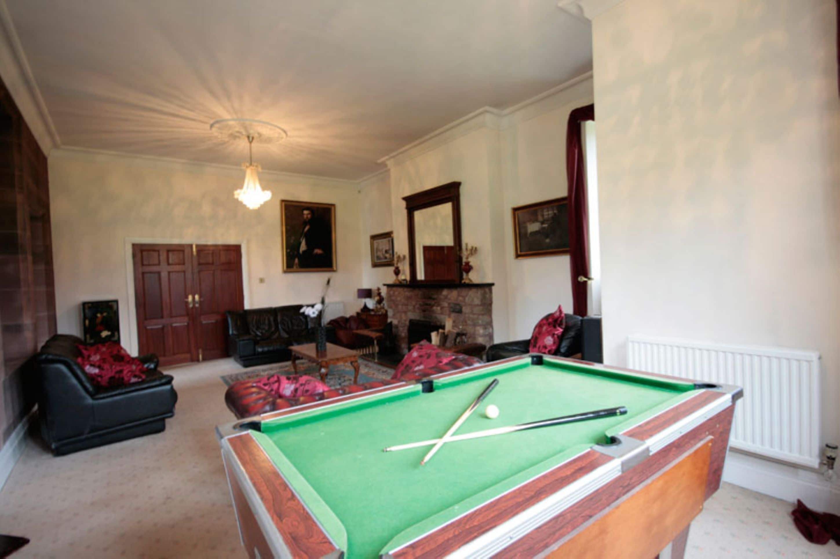 Una sala de billar con mesa de billar, chimenea y una zona de estar acogedora con sofás y otra chimenea.