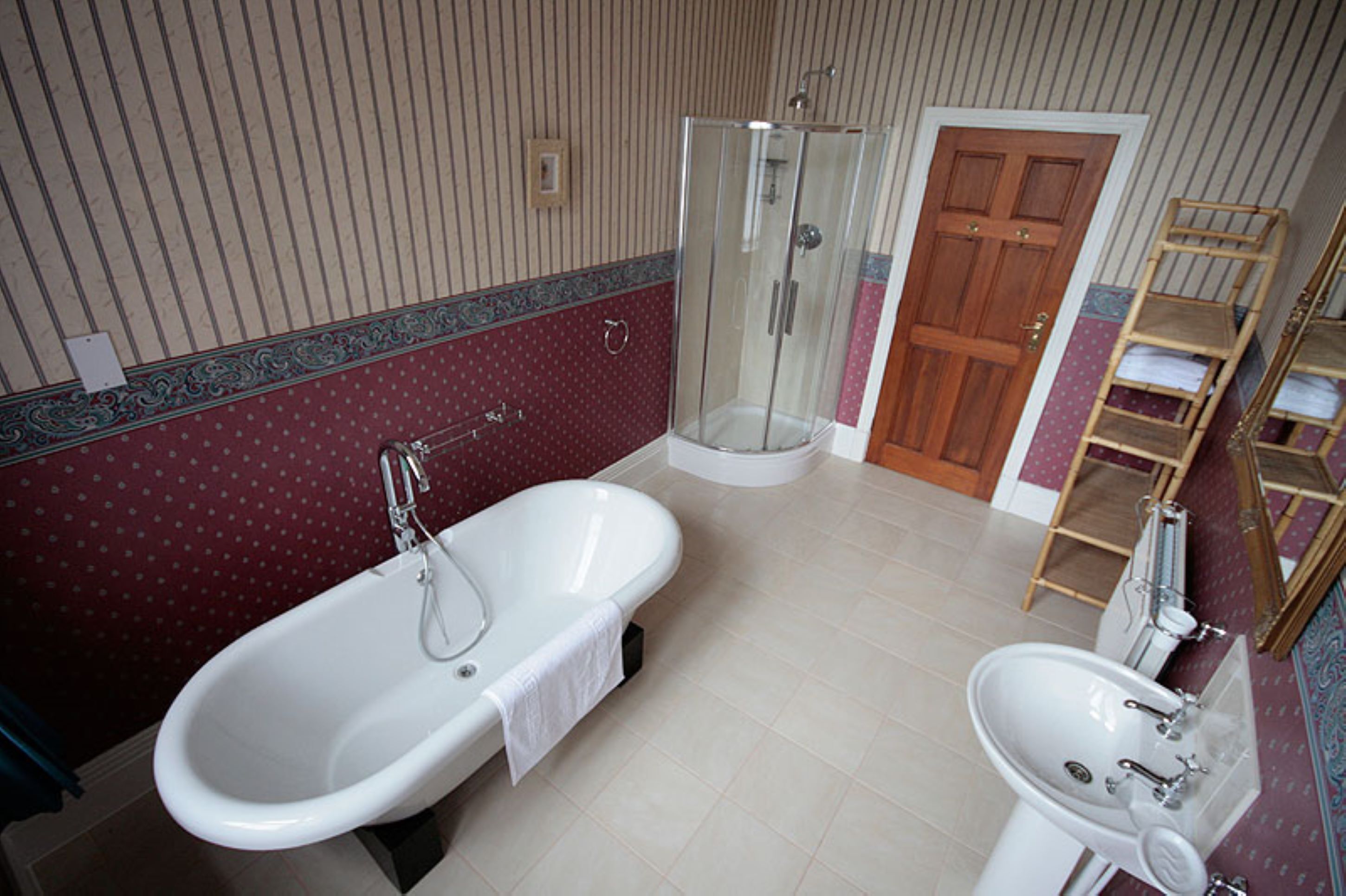 Un baño con una bañera independiente, ducha con cerramiento de vidrio, lavamanos y estante de madera.