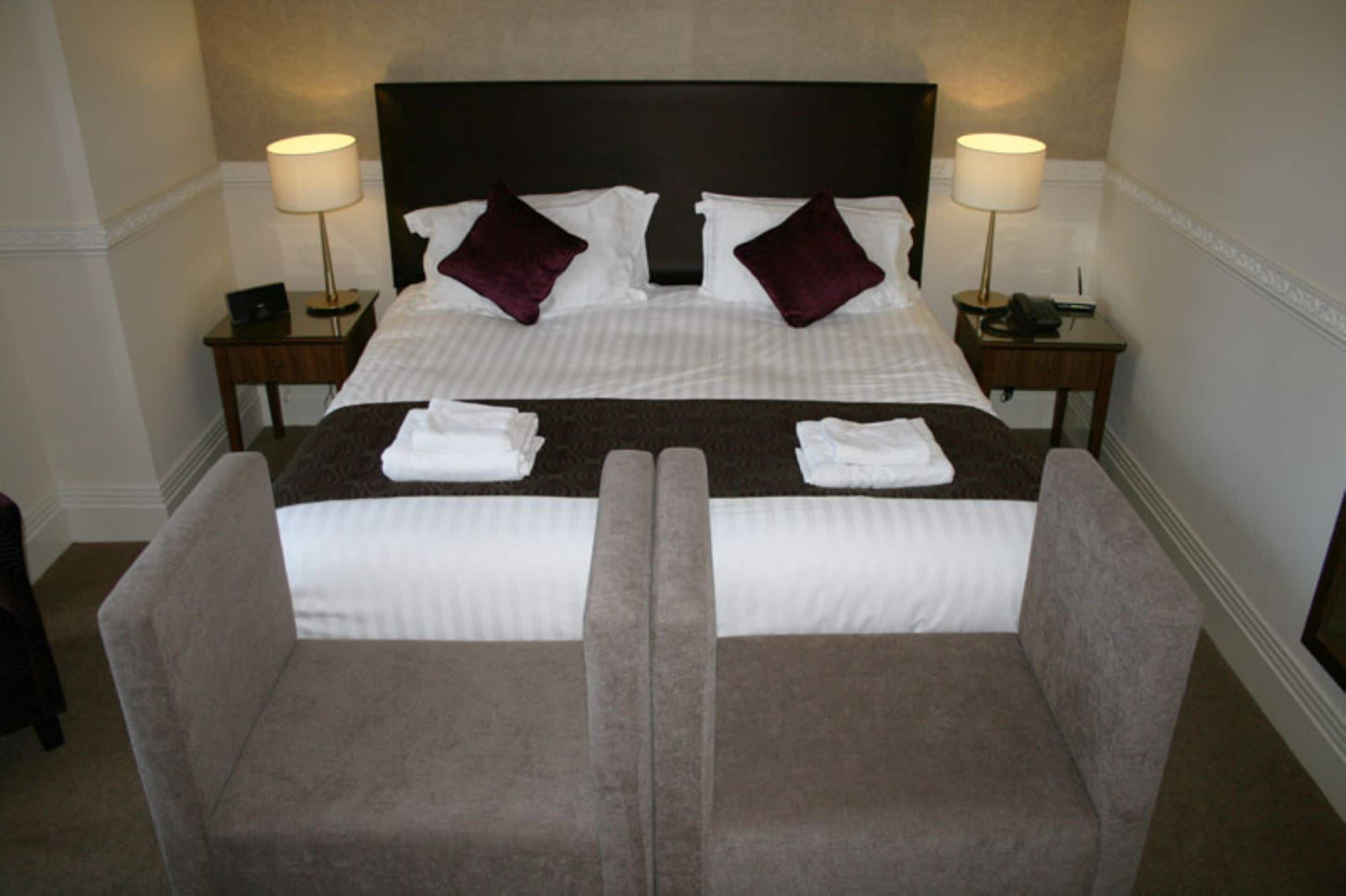 Un lit bien fait, avec des oreillers, deux tables de chevet avec des lampes et une paire de fauteuils.