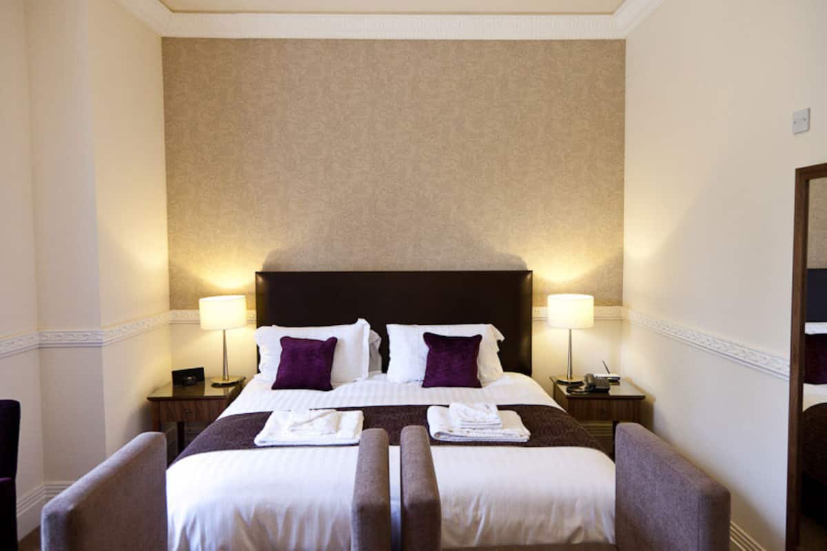 A hotel room with a large bed, two bedside tables with lamps, a chair, and a mirror on the wall.