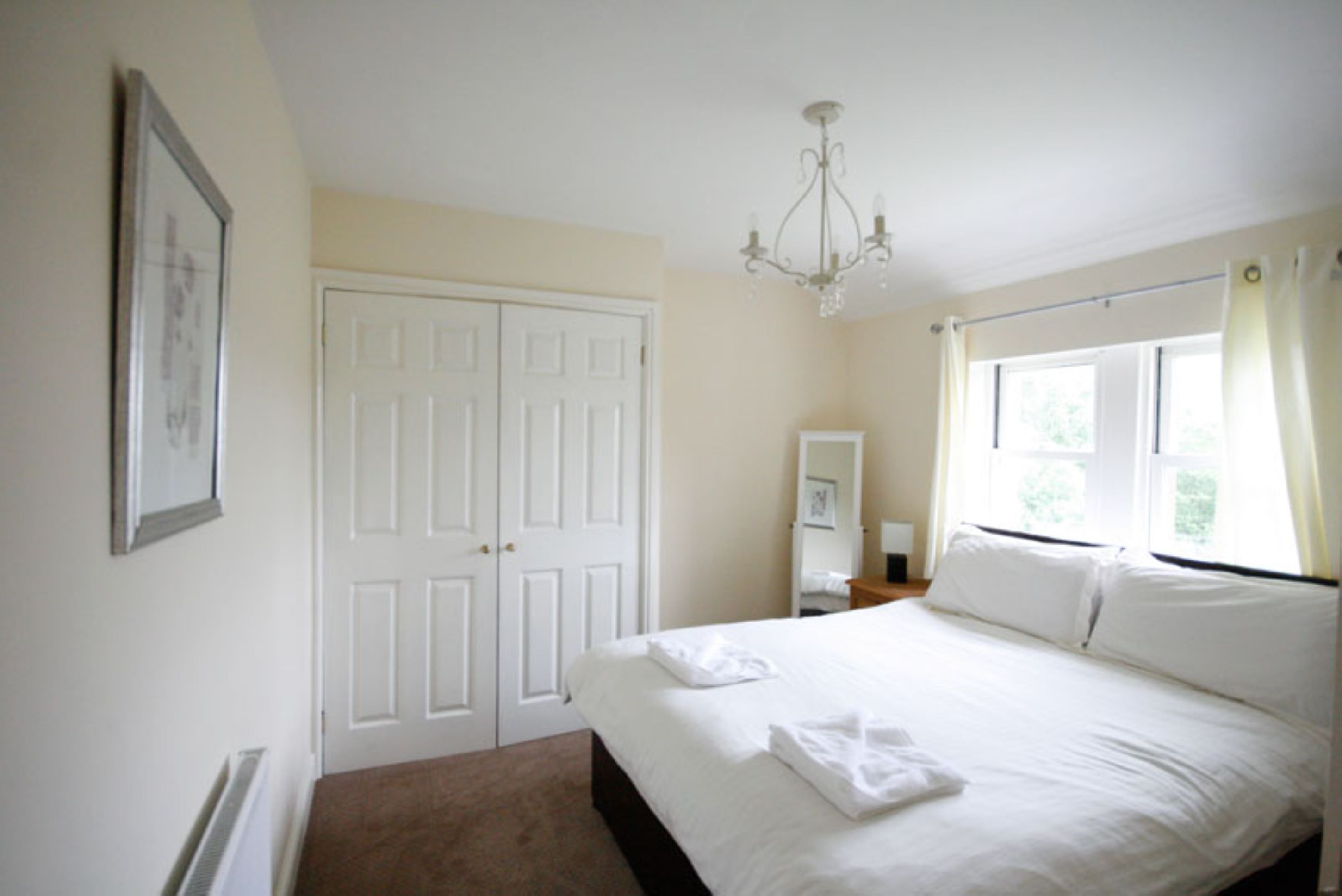 A bedroom with a bed, a chandelier, a window with curtains, and a door.