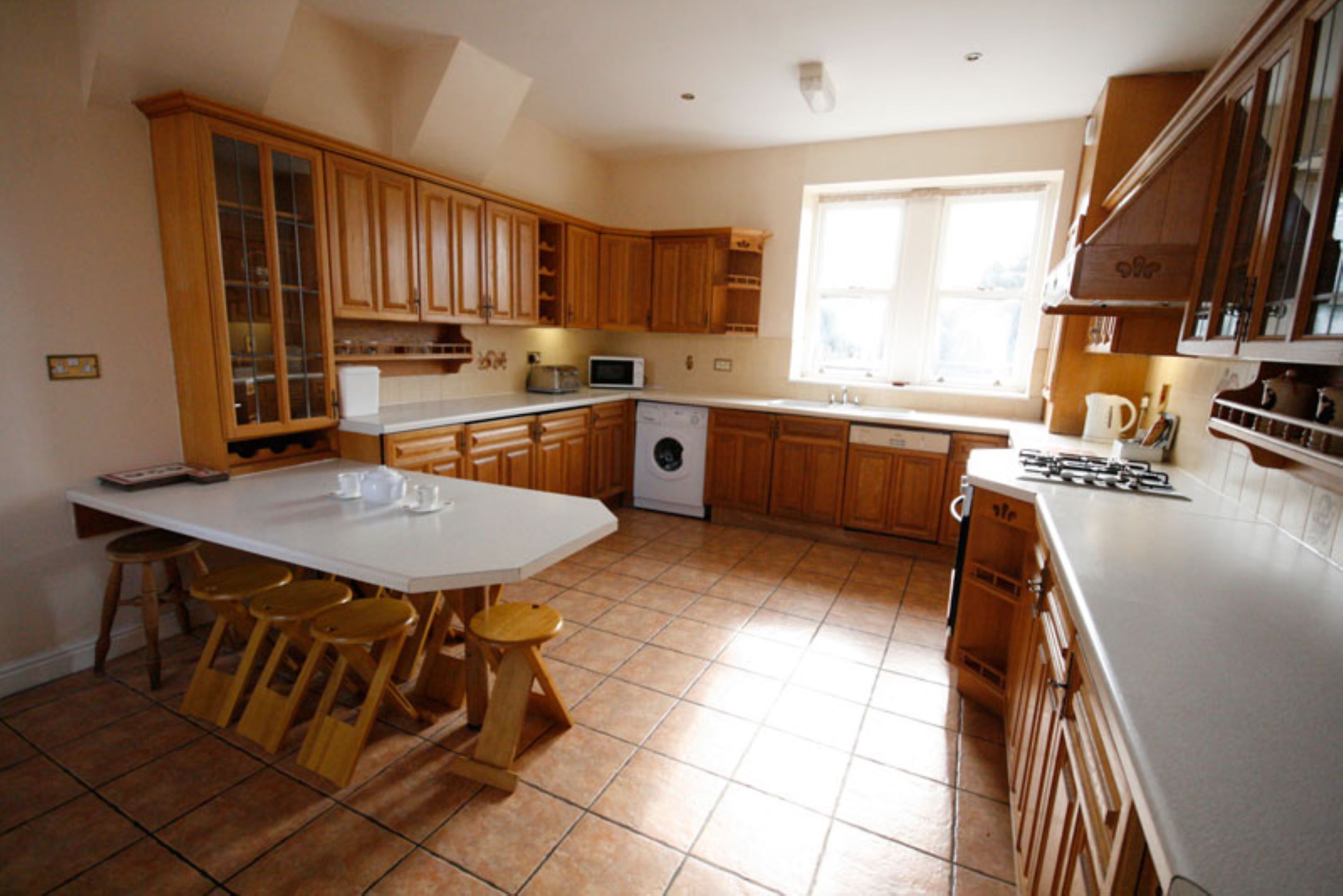 A kitchen with wooden cabinets, a white countertop, a washing machine, and a window providing natural light.