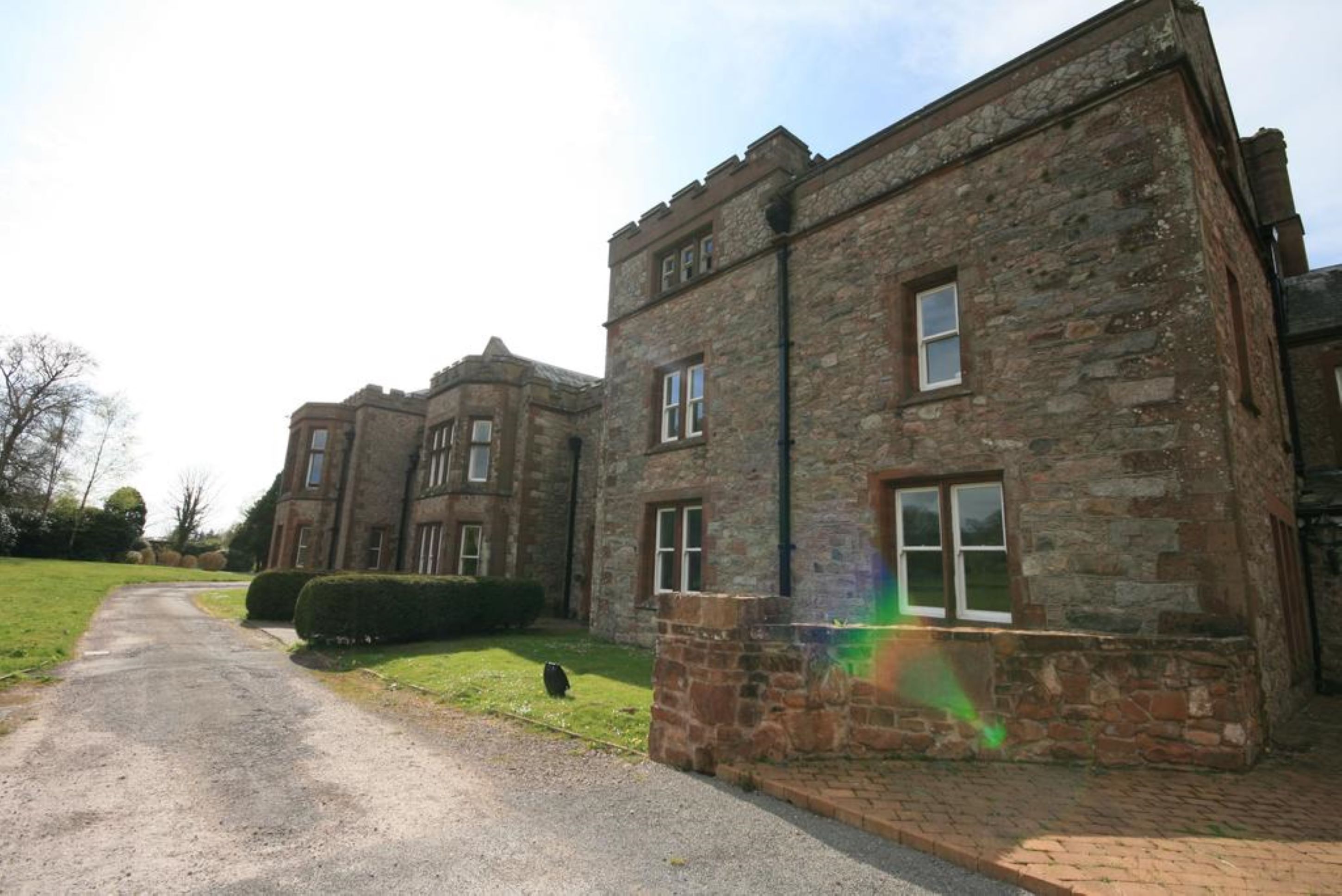 A stone building with a symmetrical facade, multiple windows, and a paved driveway leading to it.