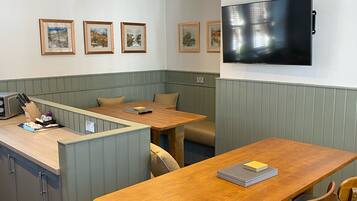 Un comedor con mesa y sillas de madera, una pequeña área de cocina con lavamanos y encimera, y un televisor de pantalla plana montado en la pared.