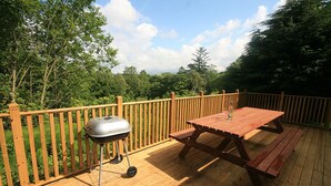 Une terrasse en bois avec un barbecue et une table de pique-nique, entourée d’une clôture en bois et d’arbres.