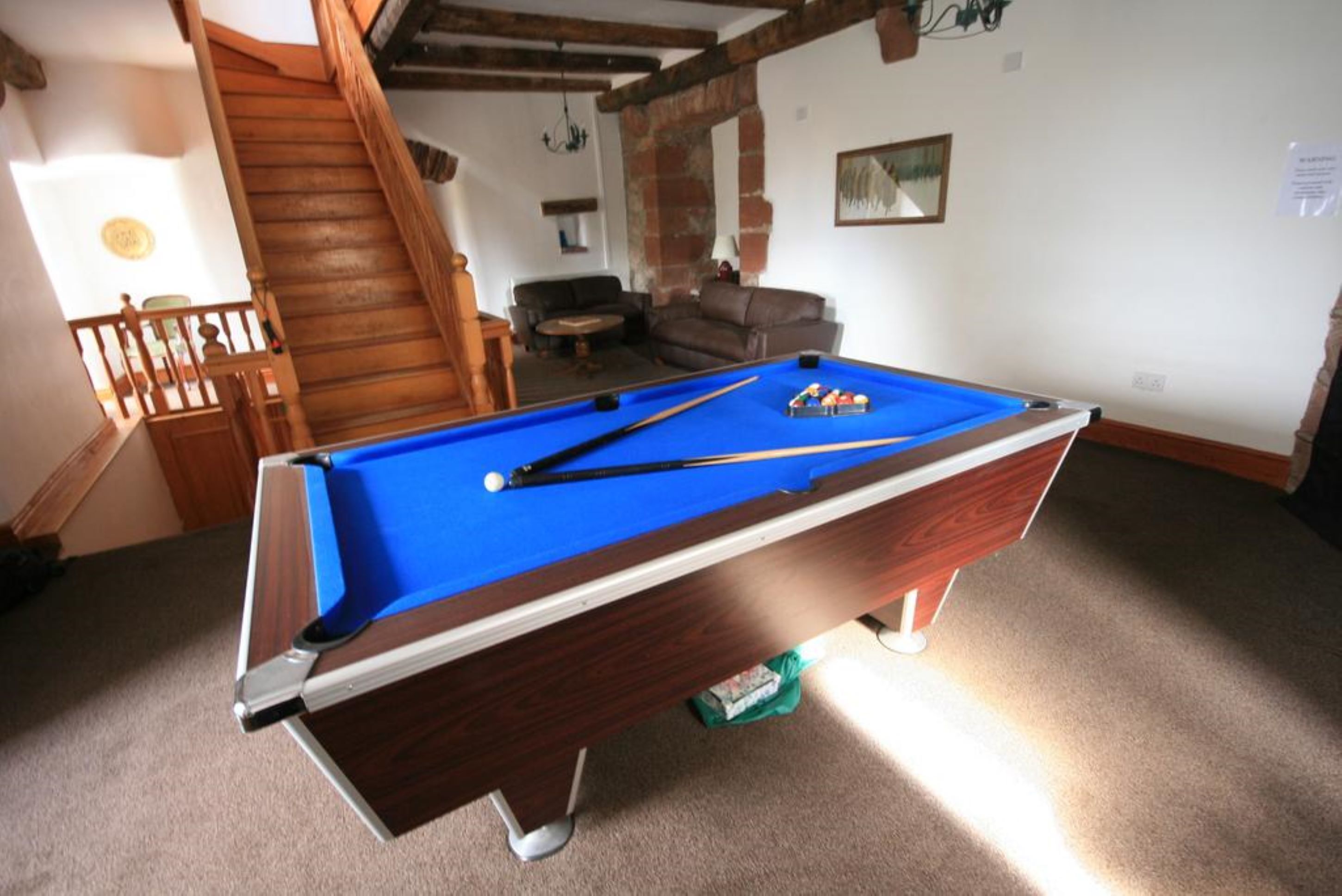 A pool table in a room with a staircase, a sofa, and a painting on the wall.