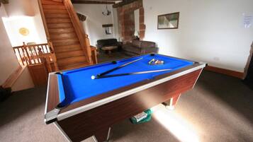 A pool table in a room with a staircase, a sofa, and a painting on the wall.