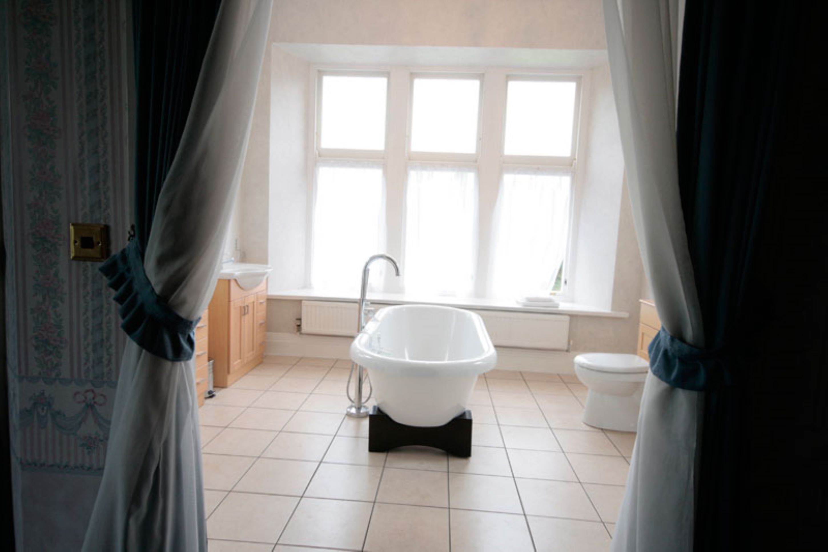 A bathroom with a freestanding bathtub, a toilet, and a window with curtains.
