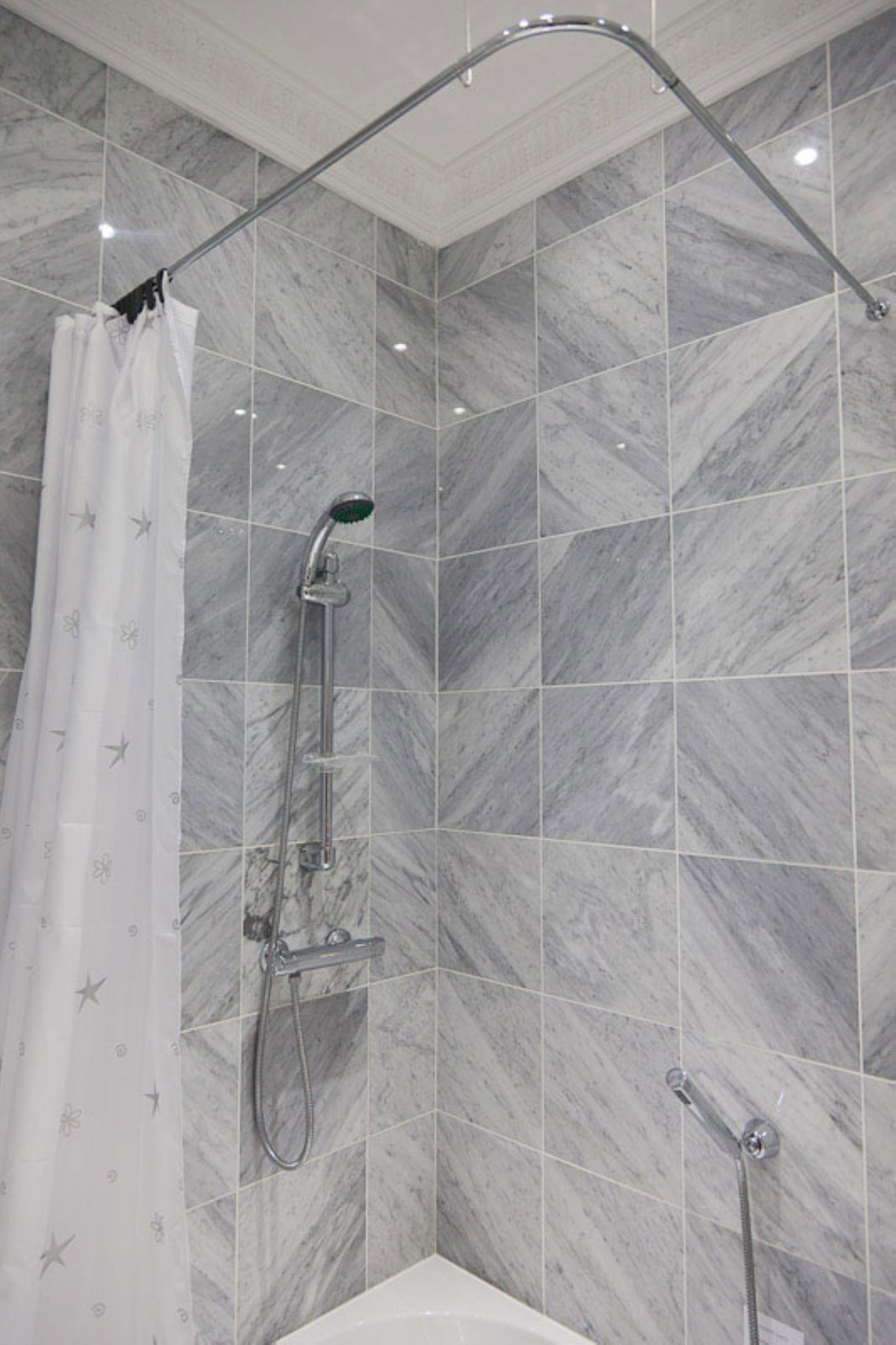 A shower area with a curved showerhead, a handheld showerhead, and a shower curtain with a star pattern.