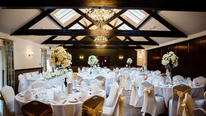 Une salle de banquet avec des tables rondes, des nappes blanches et des chaises ornées de rubans dorés.