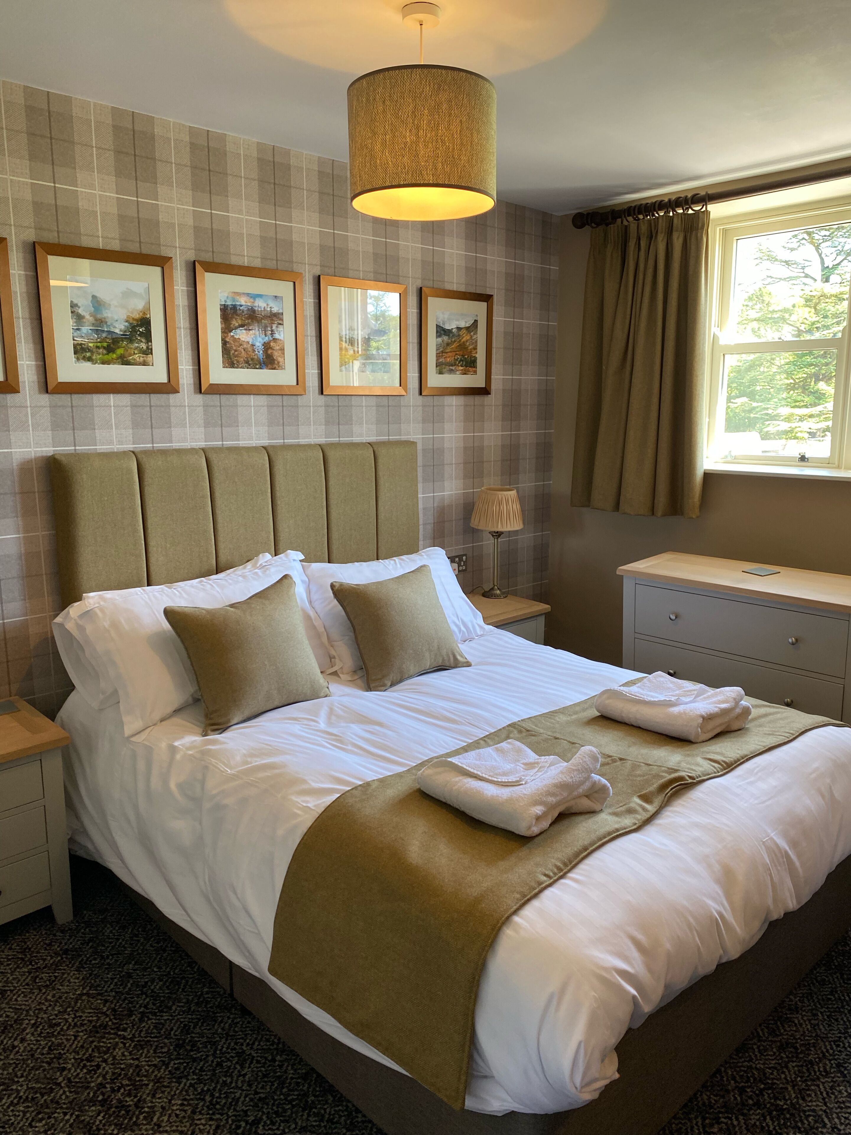 A neatly made bed with white linens and beige pillows, a bedside lamp, and framed artwork on the wall.