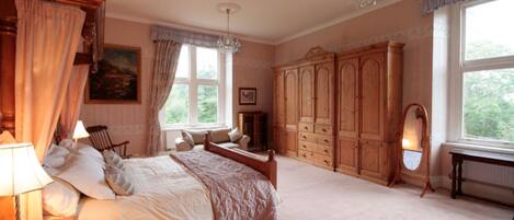 A bedroom with a large bed, wooden wardrobe, and a window with curtains.