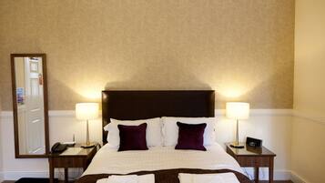 A hotel room with a large bed, two bedside tables, a nightstand, a mirror, and a door.
