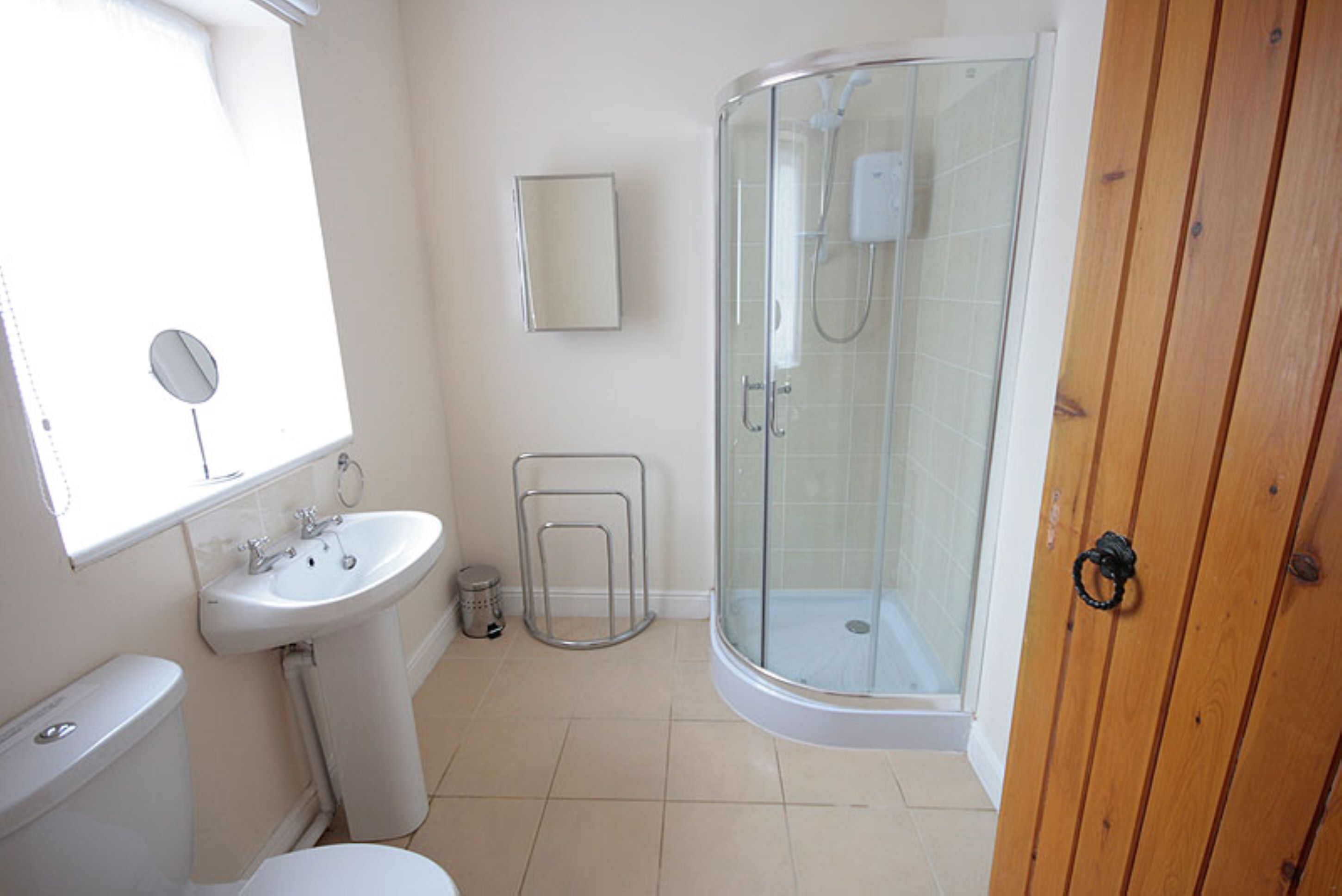 Ein Badezimmer mit Toilette, Waschbecken, Dusche und einer Holztür.