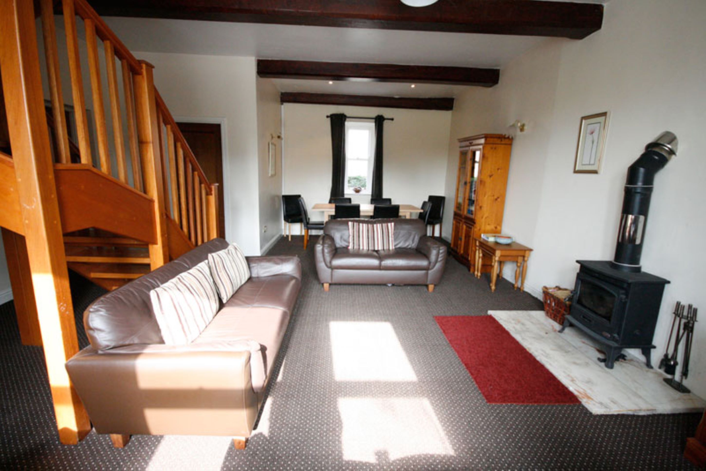 A living room with a wooden staircase, a sofa, a dining table with chairs, a fireplace, and a red rug.