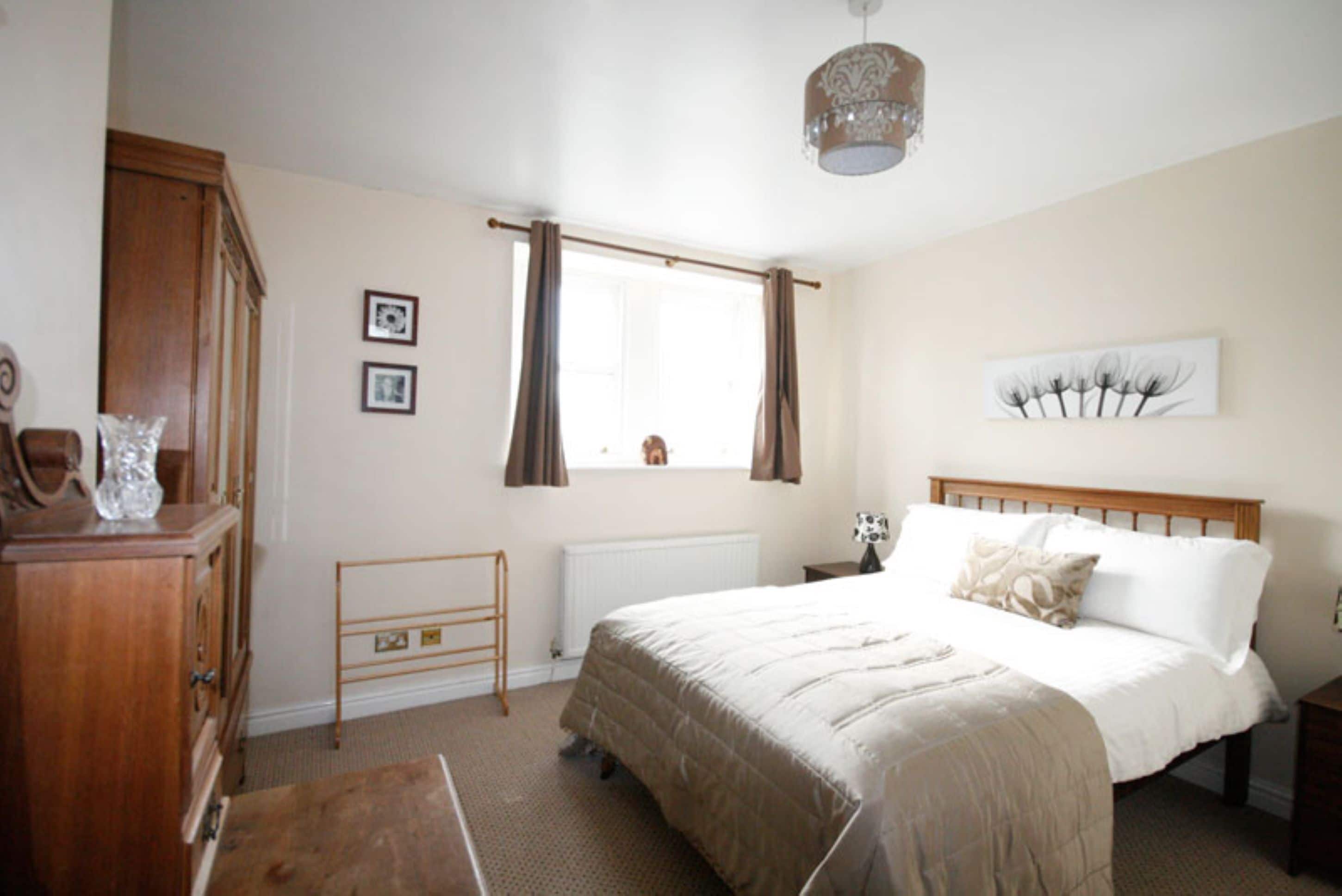 A bedroom with a wooden bed, a radiator, a window with curtains, and a wooden dresser.