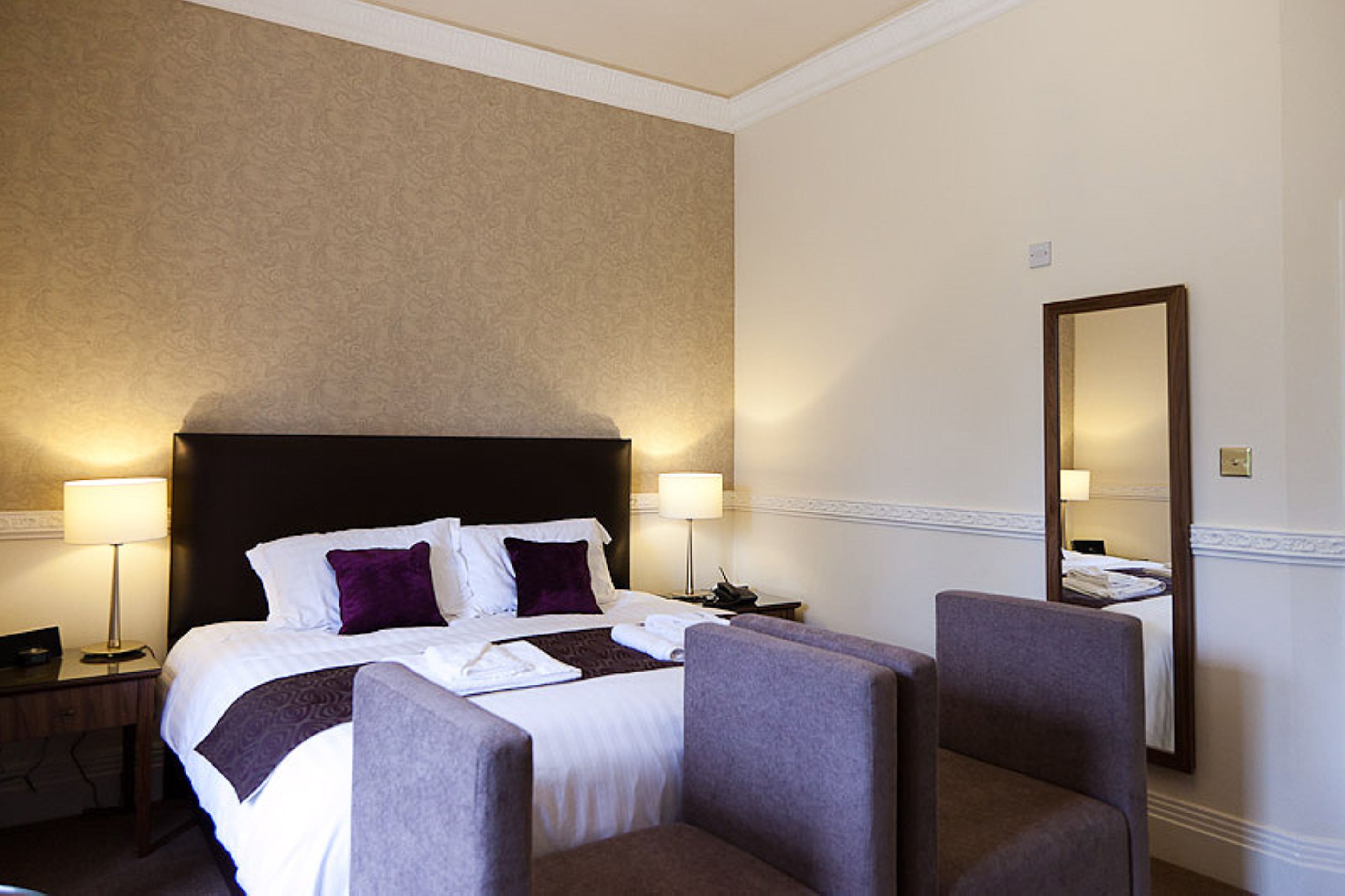 Habitación de hotel con una cama grande, dos lámparas de noche, una mesita de noche, una silla y un espejo en la pared.