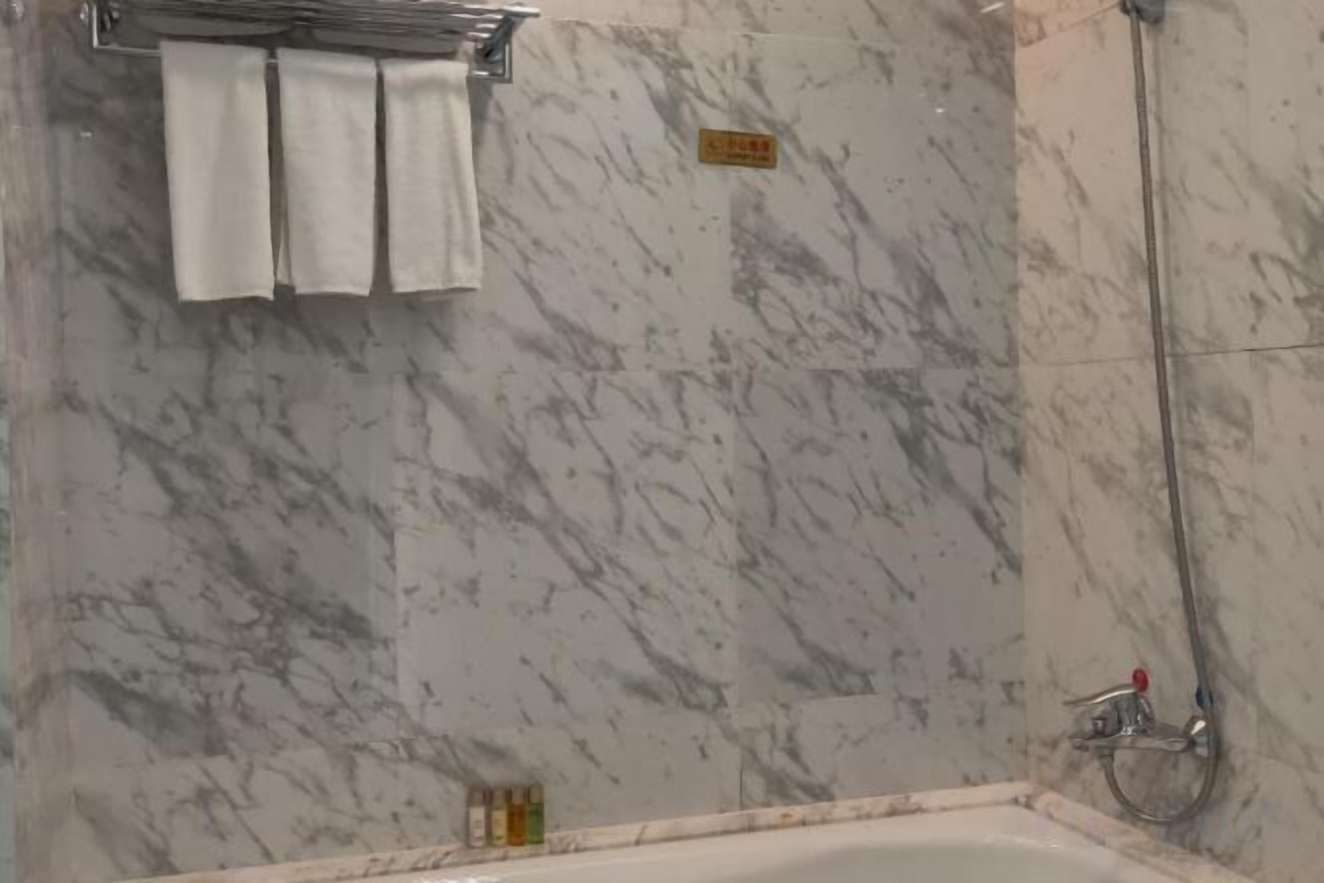 Un baño con pared de mármol, una bañera y una ducha.