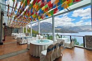 Ein Restaurant mit runden Tischen und Stühlen, einer Glasdecke und Blick auf Berge und einen See.