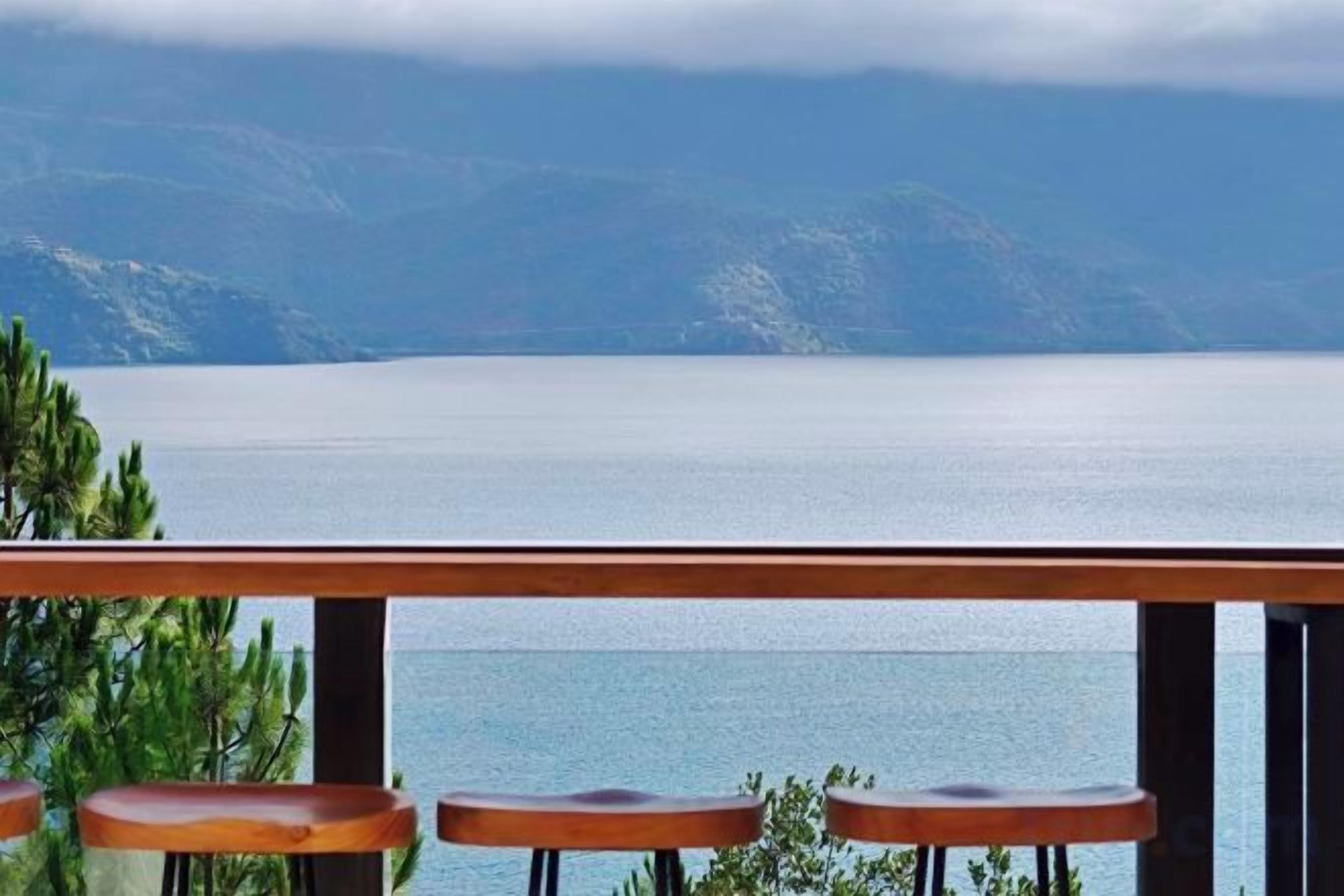 A view of a lake with mountains in the background, a wooden railing, and three wooden stools.