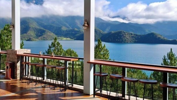 A terrace with bar stools overlooking a lake and mountains. - Silver Lake Island Hotel At Lugu Lake, Yunnan (Lijiang)
