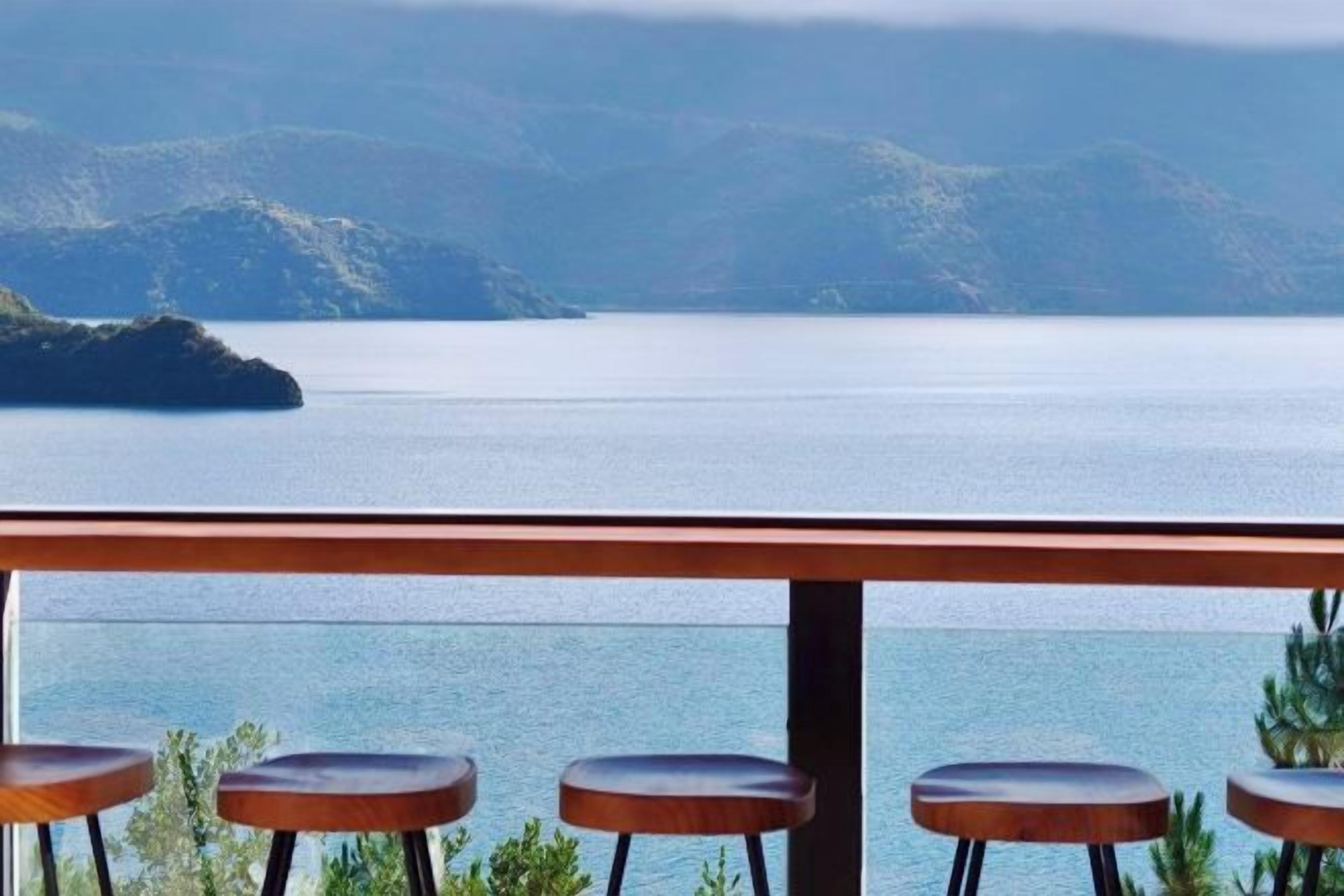 Een bar met krukken en uitzicht op een rustig meer en verre heuvels.