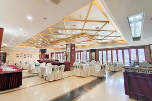 A banquet hall with tables set for events, a stage, and a large window providing natural light.