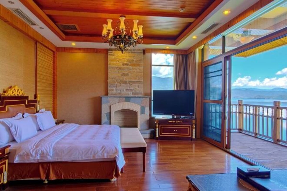 A bedroom with a bed, a fireplace, a TV, and a balcony with a view.