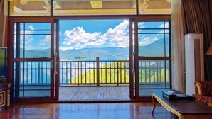 A room with large sliding glass doors leading to a balcony with a mountain view. - Silver Lake Island Hotel At Lugu Lake, Yunnan (Lijiang)