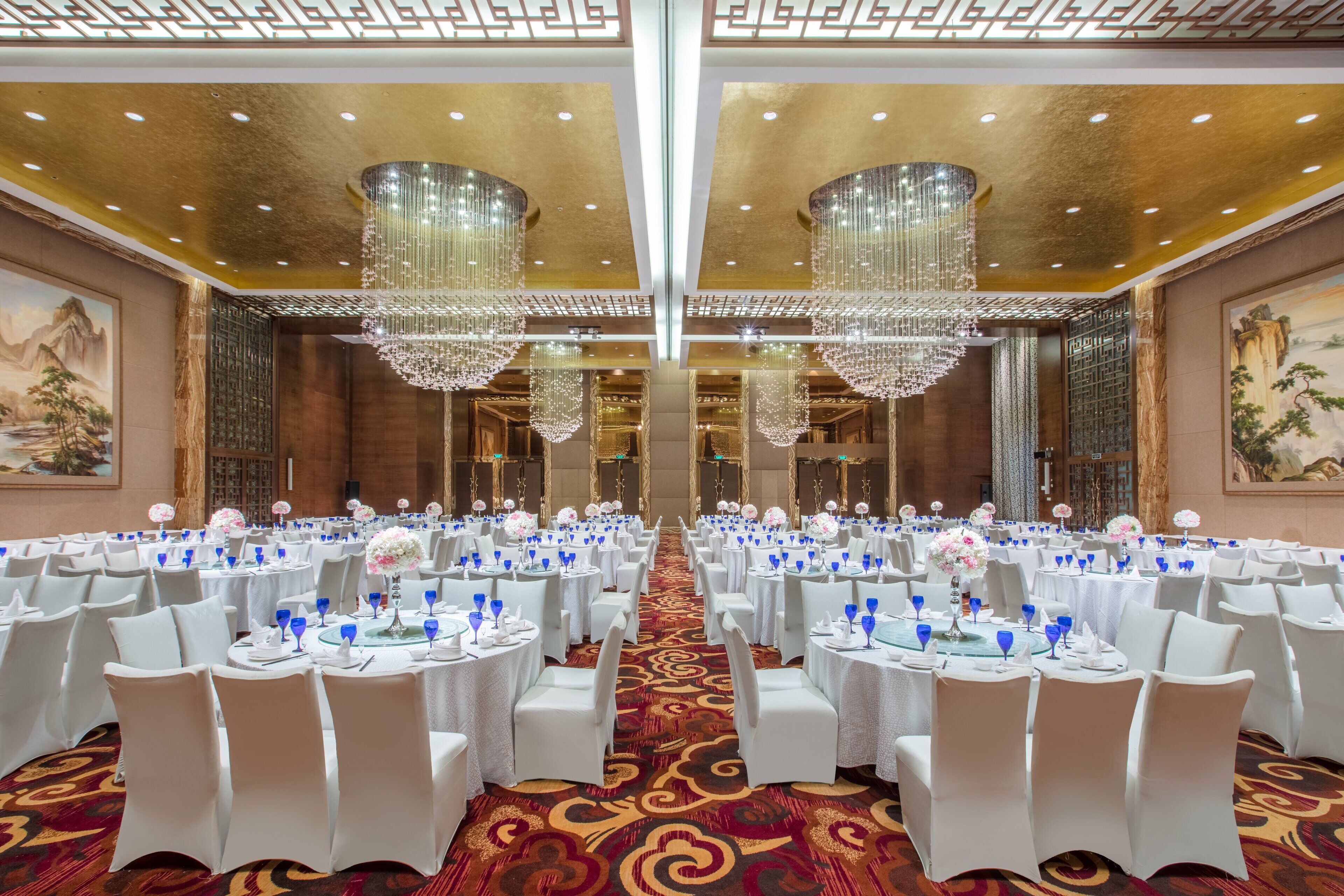 Une salle de banquet avec des tables rondes, des chaises blanches et des lustres.