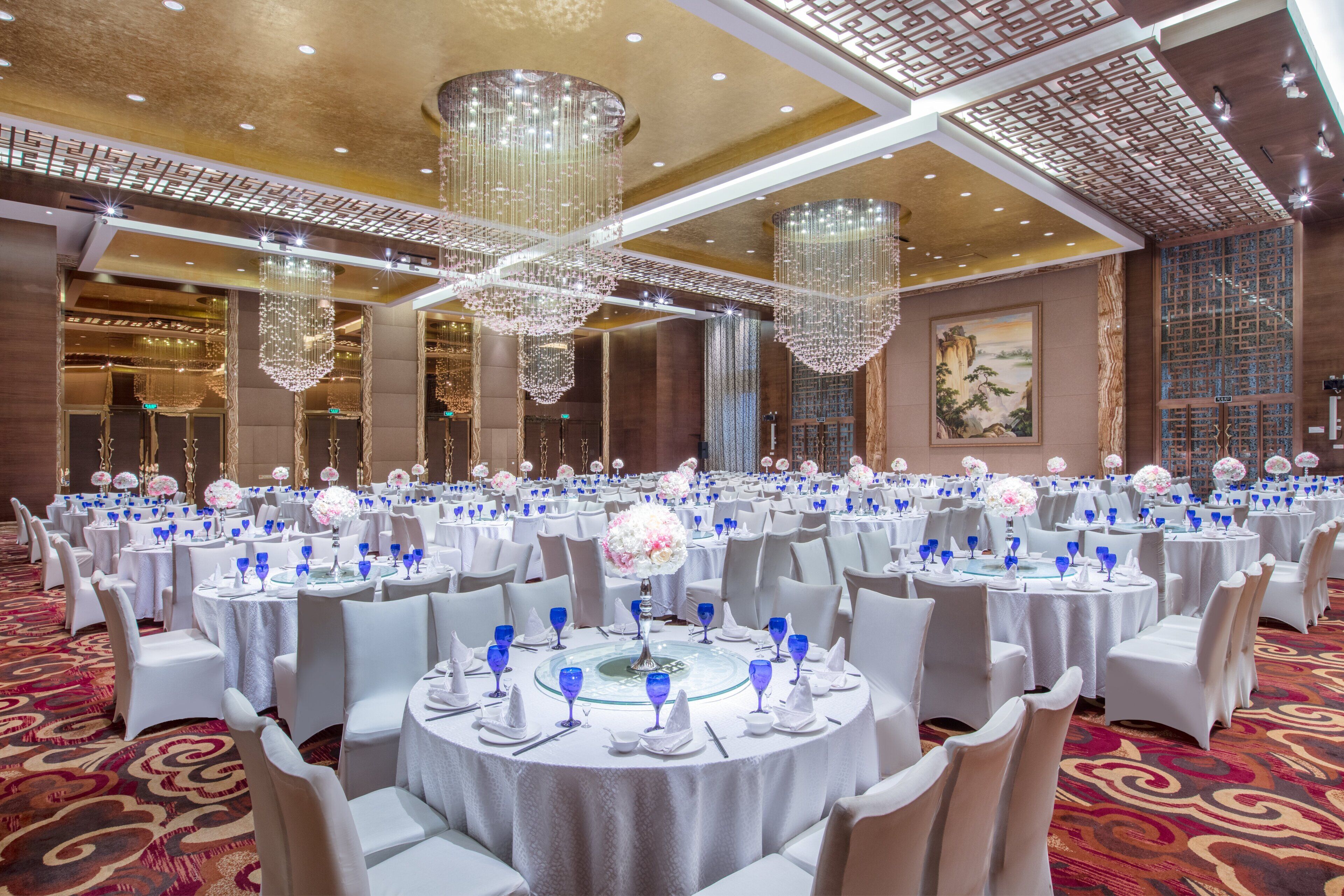 A banquet hall with round tables, white tablecloths, and blue glassware.