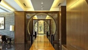 Un moderno vestíbulo de hotel con un largo mostrador de recepción de madera pulida, un área de descanso con sillas y una pared decorativa con un diseño circular.