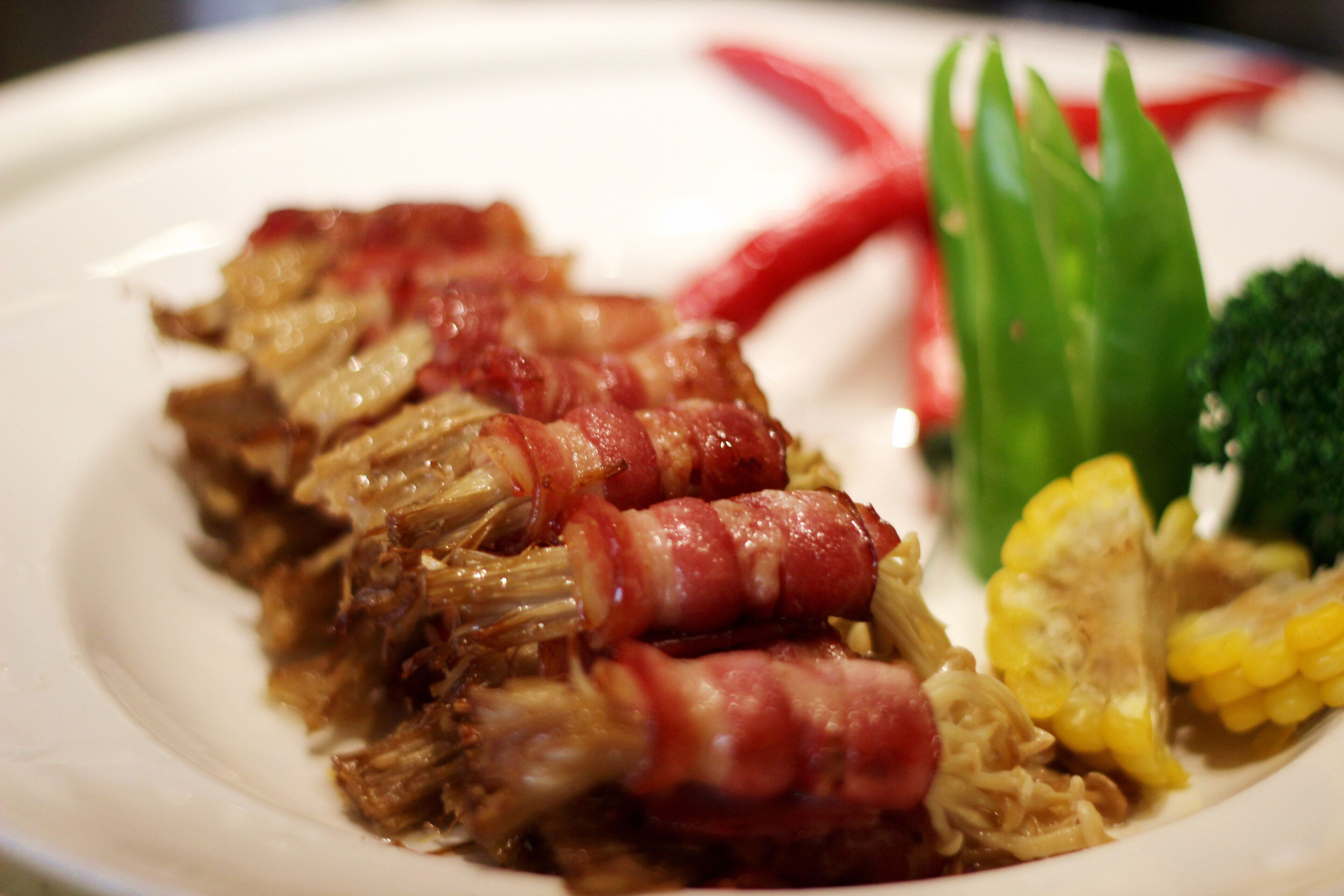 A plate with shredded meat wrapped in bacon, green vegetables, and corn.