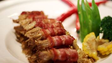 A plate with shredded meat wrapped in bacon, green vegetables, and corn.