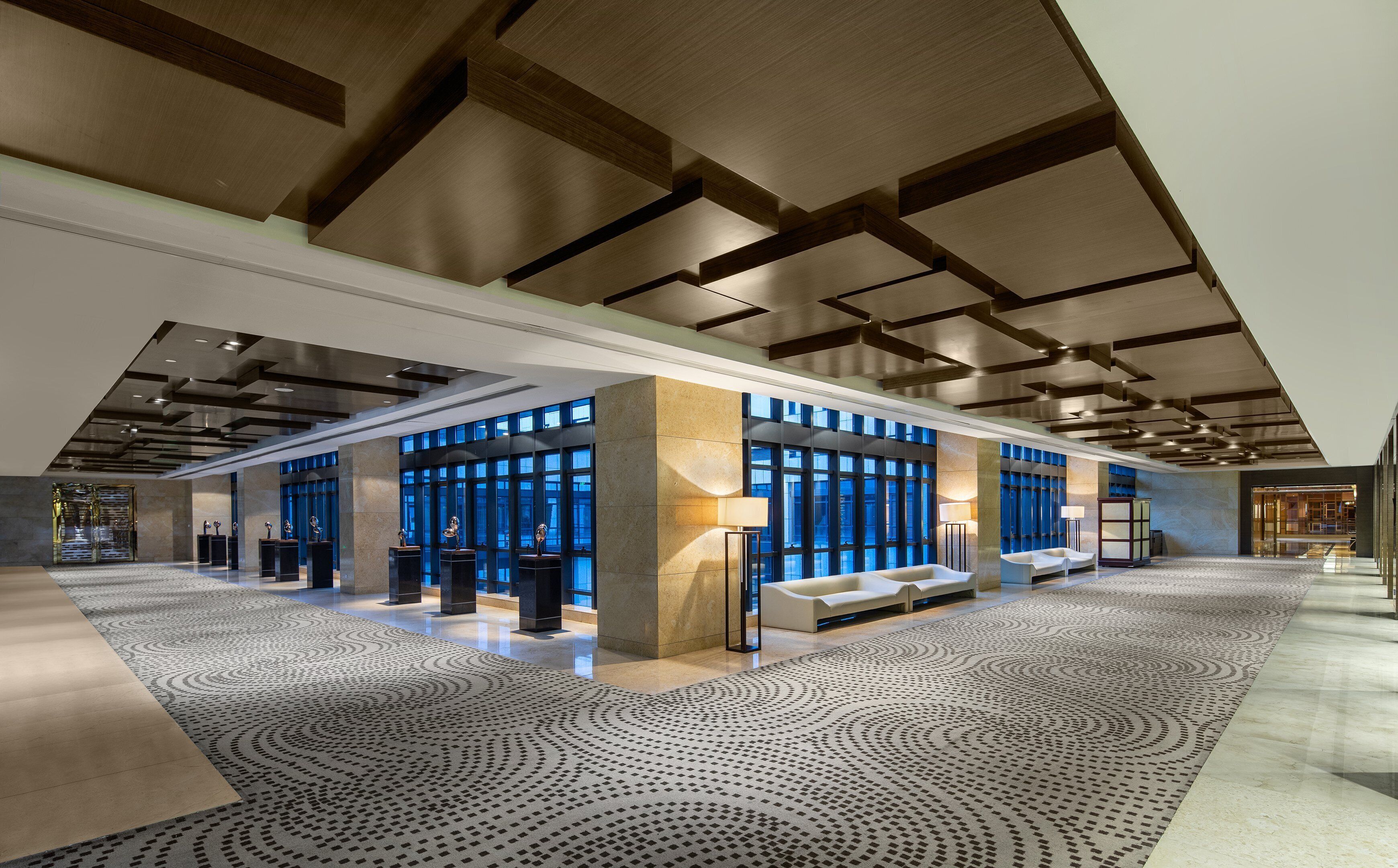 A spacious lobby with a high ceiling, large windows, and a patterned carpet.