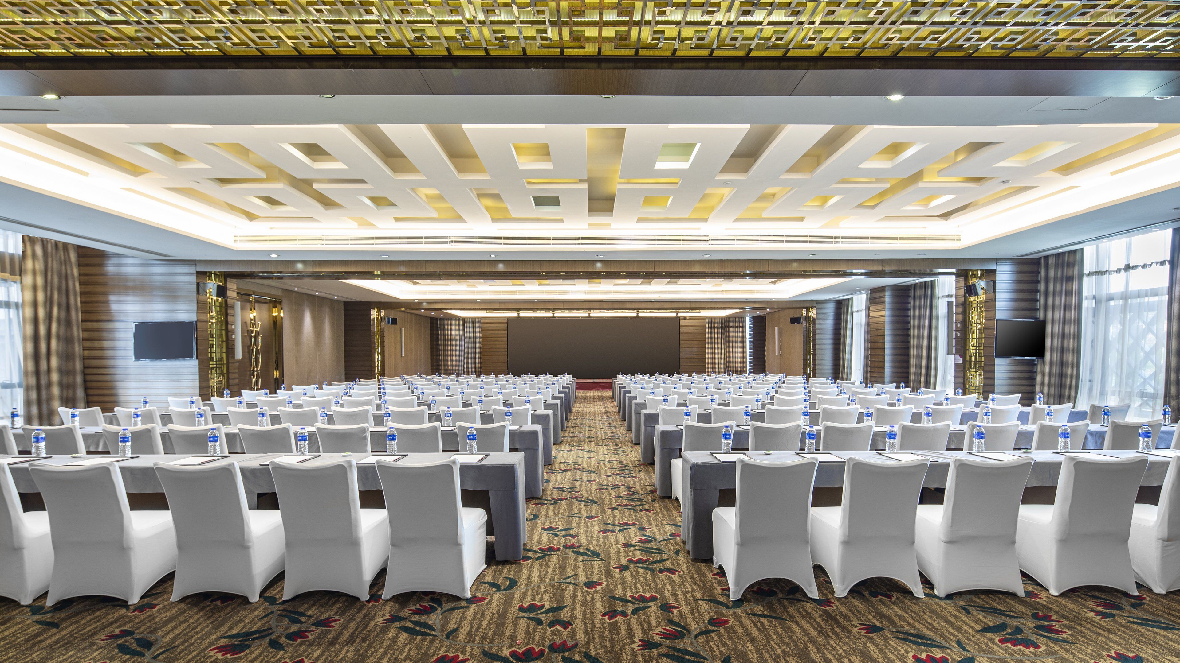 A conference room with rows of white chairs, a patterned carpet, and a modern ceiling design.