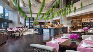 A spacious hotel lobby with a central bar area, high ceilings, and hanging greenery.