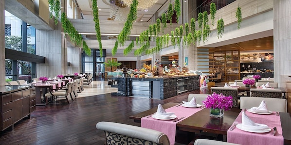 Un hall d’hôtel spacieux avec un bar central, de hauts plafonds et des plantes suspendues.