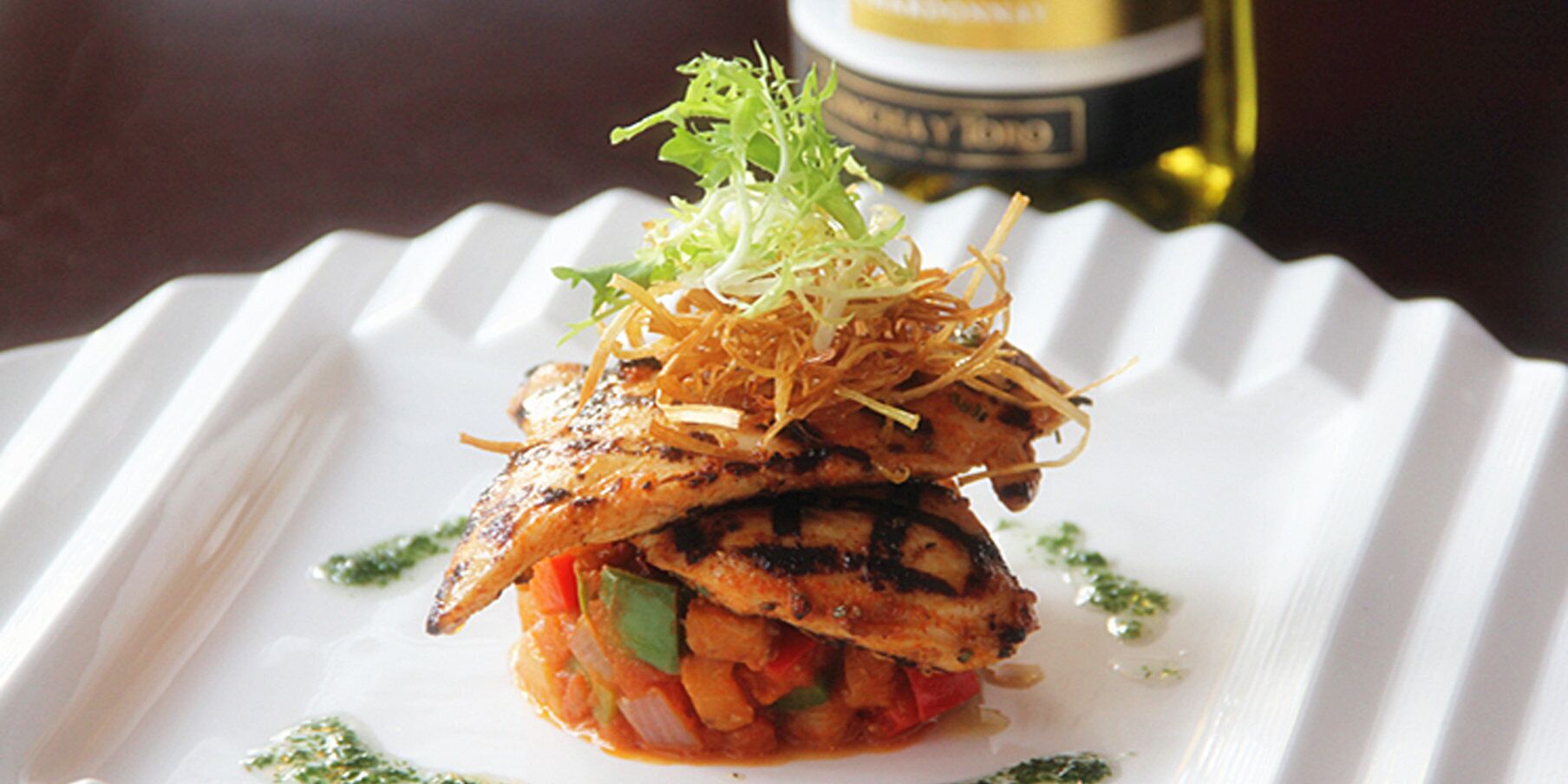 A dish with grilled chicken, vegetables, and garnishes on a white plate.