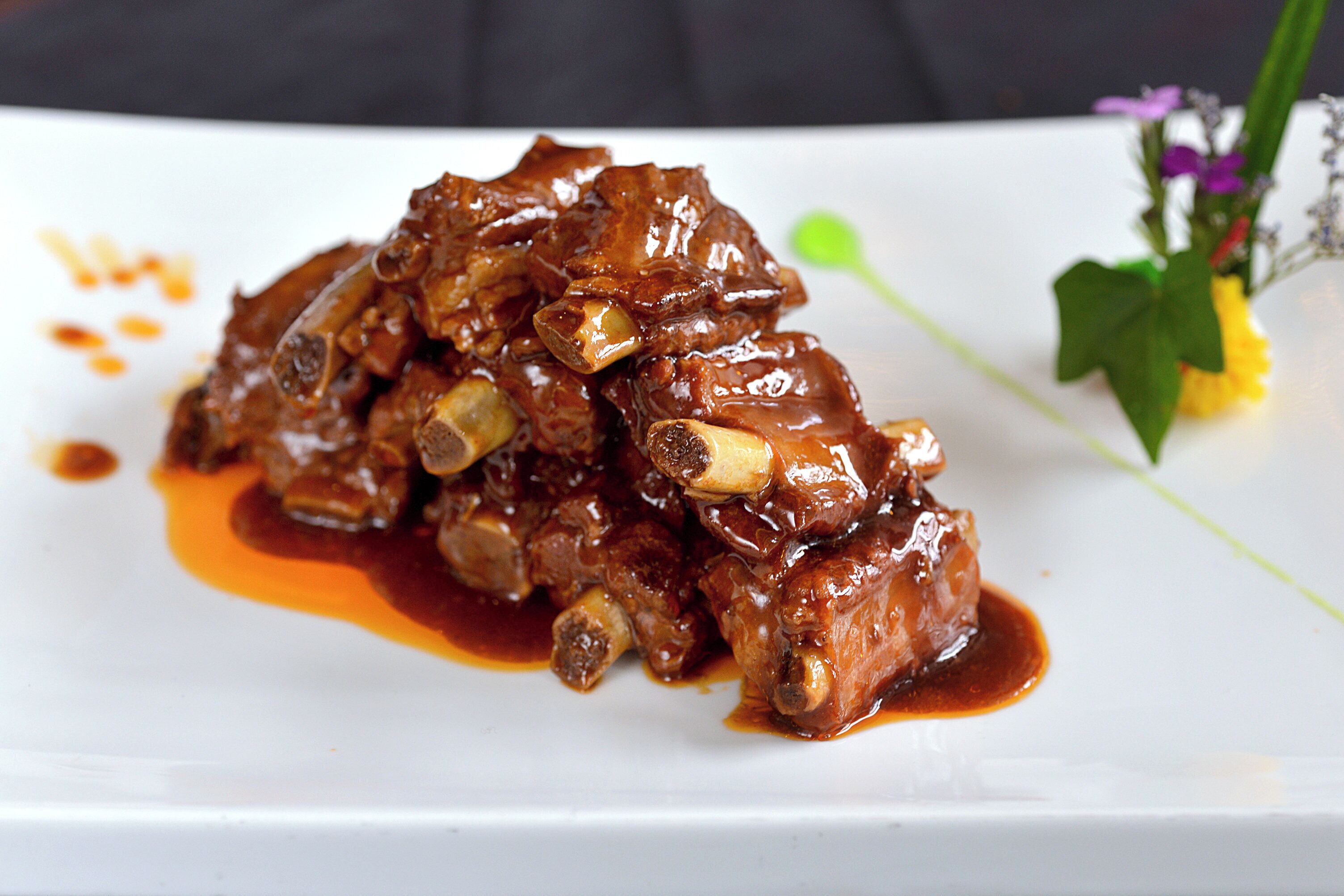 A dish of braised meat with a rich sauce on a white plate.