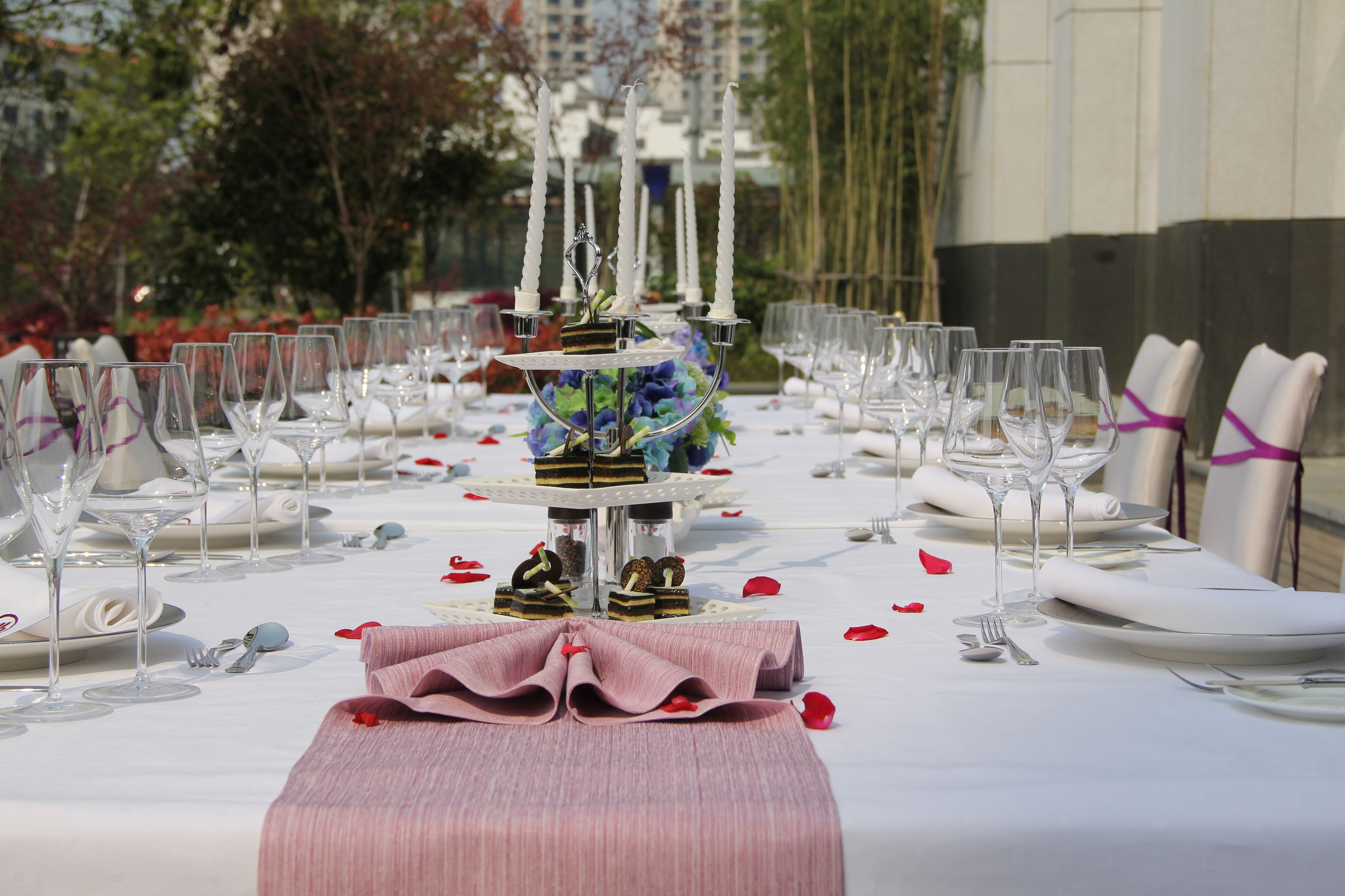 Une table de salle à manger élégante, installée à l’extérieur, recouverte de nappes blanches, agrémentée de verres et de serviettes soigneusement pliées.
