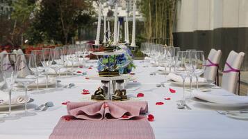 A formal outdoor dining table set with white tablecloths, glassware, and neatly folded napkins.
