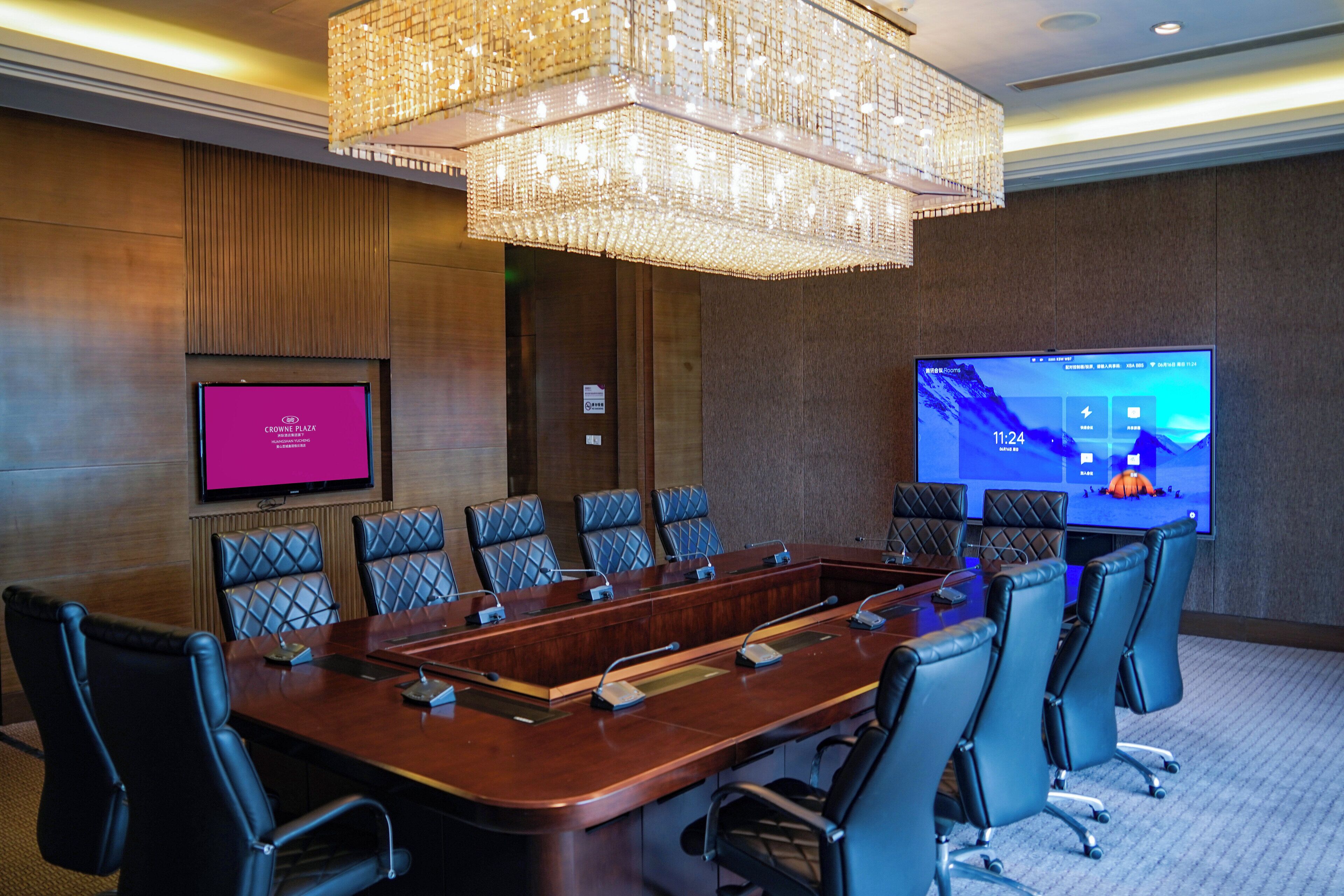 A conference room with a long table, multiple chairs, a large screen, and a chandelier.