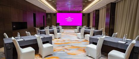 A conference room with a large screen, white chairs, and tables set up for a meeting.