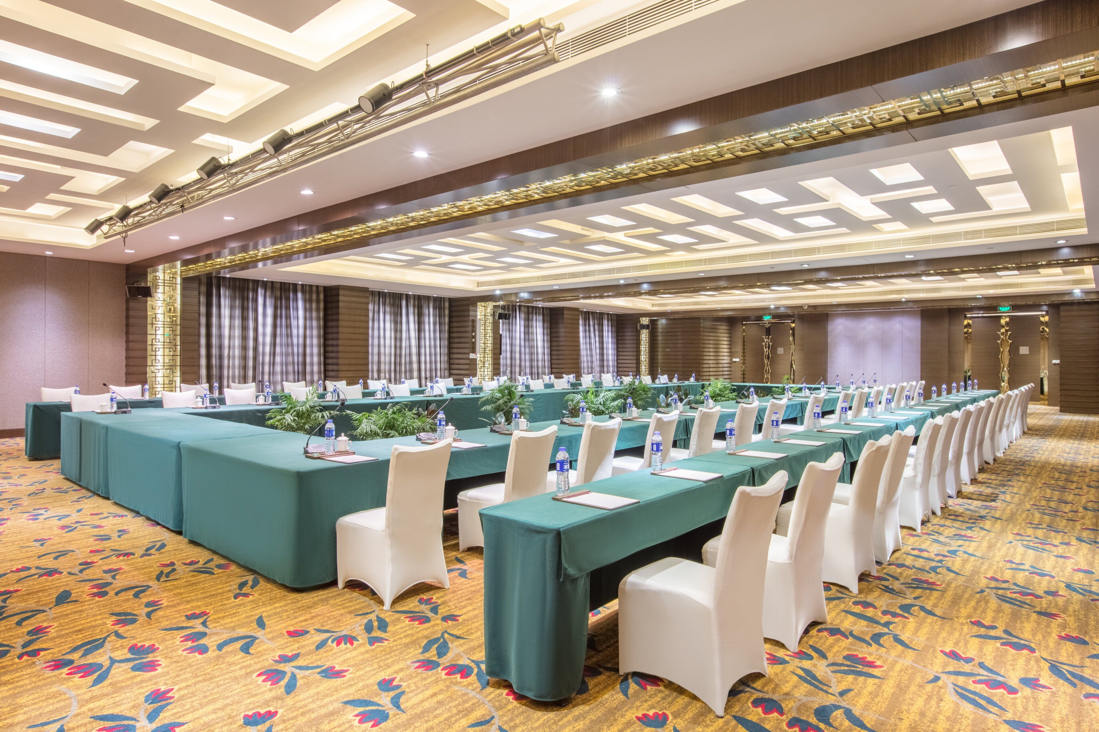 A conference room with long tables, white chairs, and a patterned carpet.