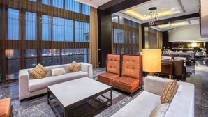 A spacious lobby with a sofa, armchairs, and a coffee table. Large windows offer a view of the cityscape.