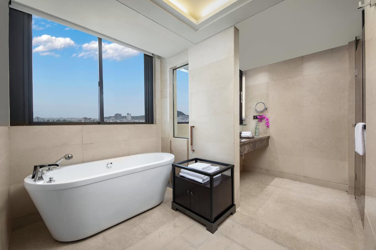A modern bathroom with a freestanding bathtub, a vanity with a mirror, and a view of the city through large windows.